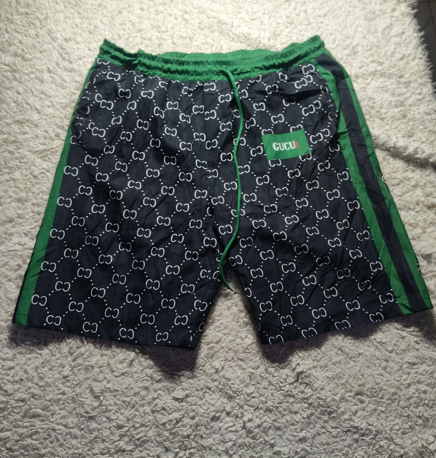 Gucci GG Supreme shorts in navy blue with green trim and white GG monogram pattern, laid flat on a white shag rug.