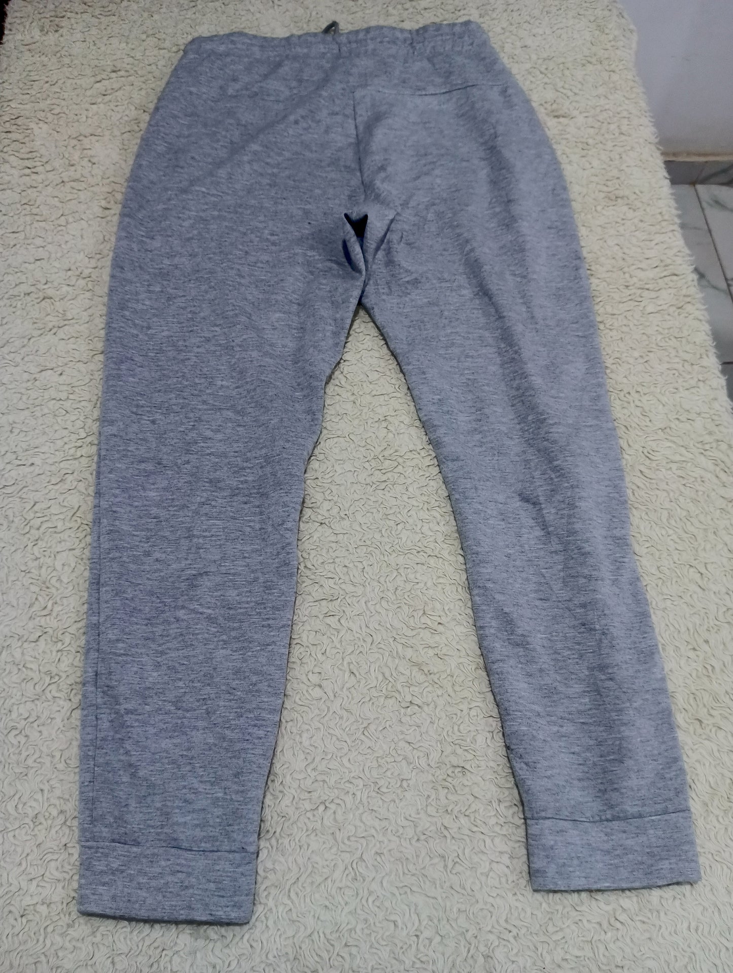 A pair of heather gray sweatpants laid flat on a beige shag rug, photographed from above. The image has a camera info overlay at the bottom.