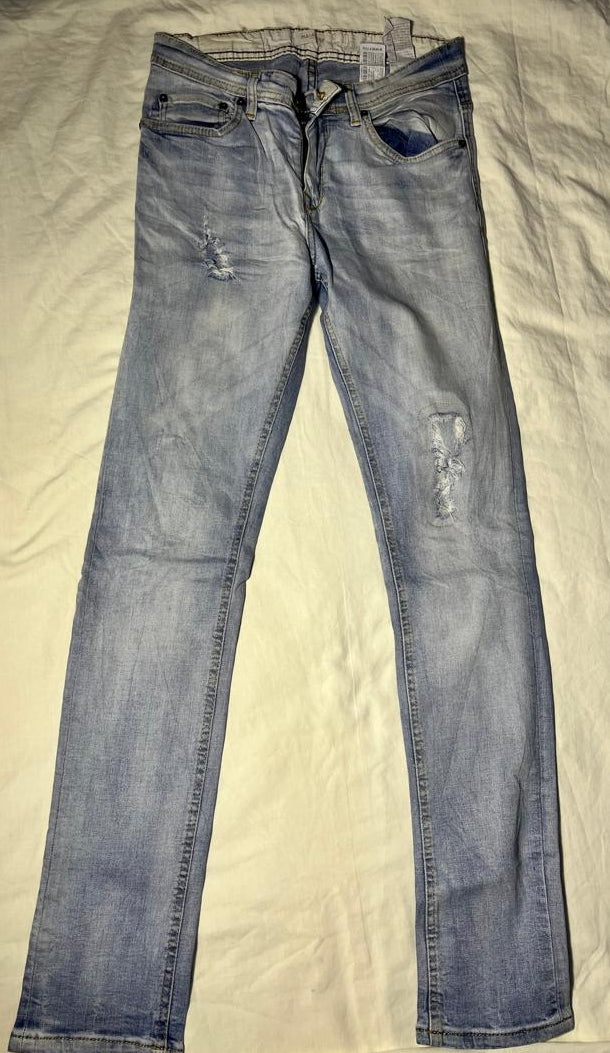 Light wash blue denim jeans with distressed rips on the thighs and knees, laid flat on a cream-colored fabric background.