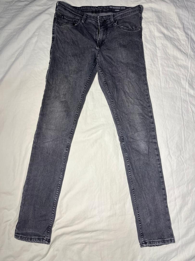 A pair of dark gray slim-fit jeans laid flat on a white fabric background.