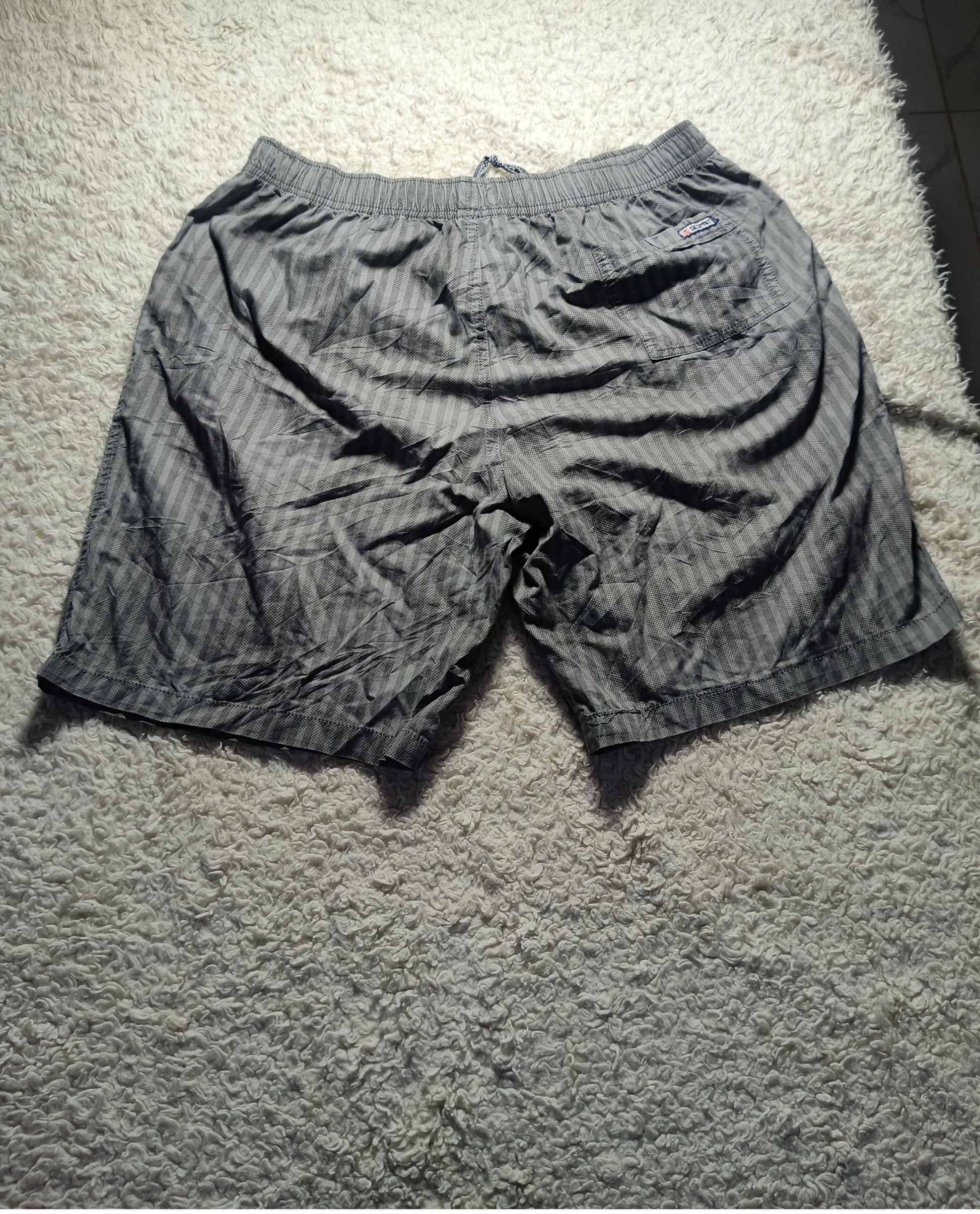 A pair of men's casual shorts with a gray and black striped pattern, laid flat on a textured white carpet.
