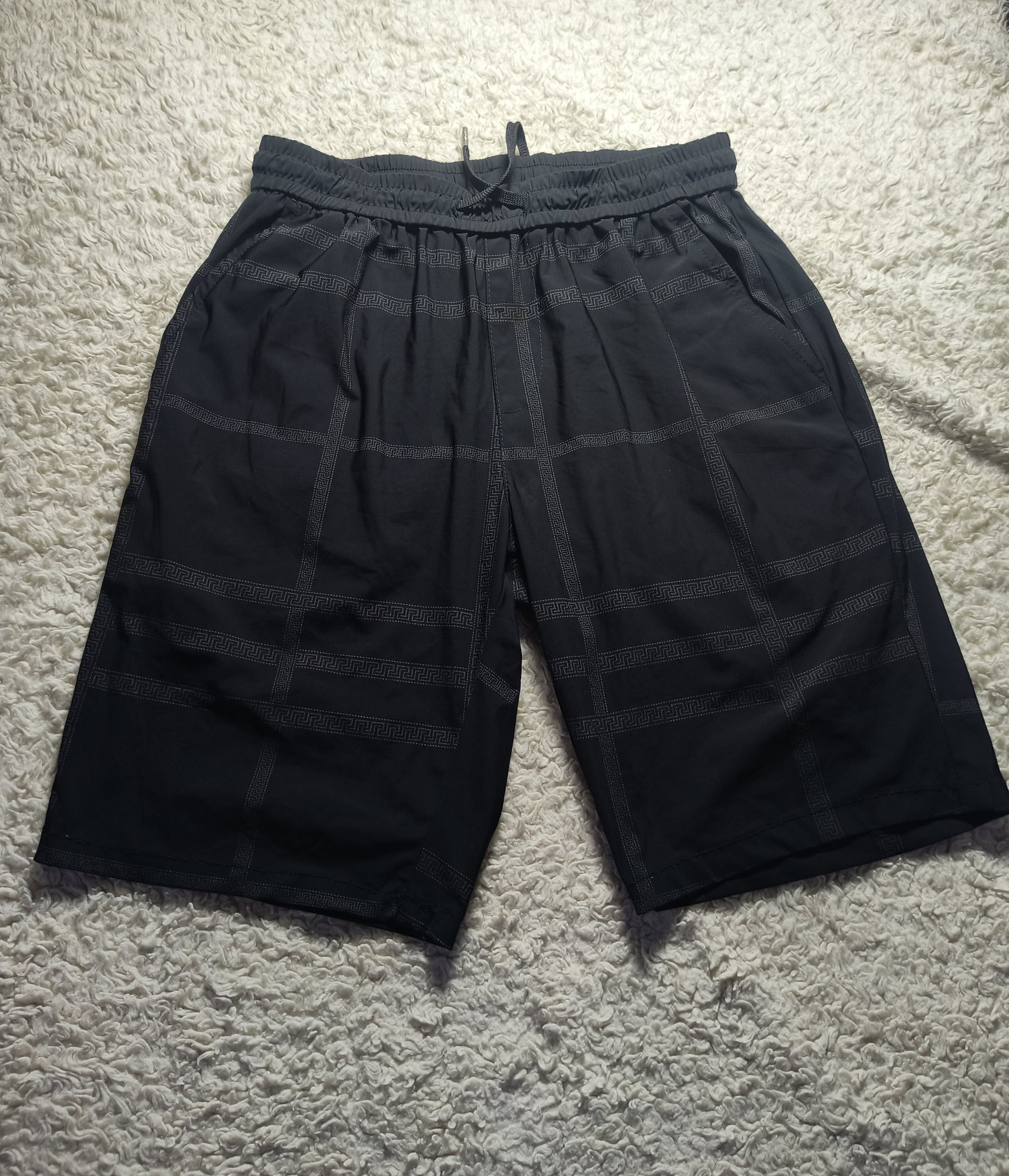 Black plaid drawstring shorts laid flat on a white shag rug, with a visible waistband and drawstring.