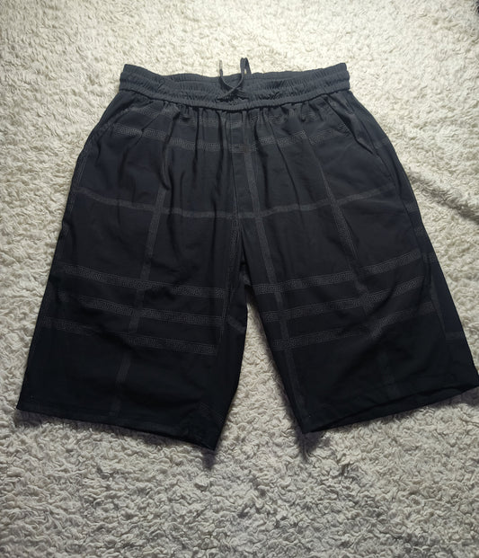 Black plaid drawstring shorts laid flat on a white shag rug, with a visible waistband and drawstring.