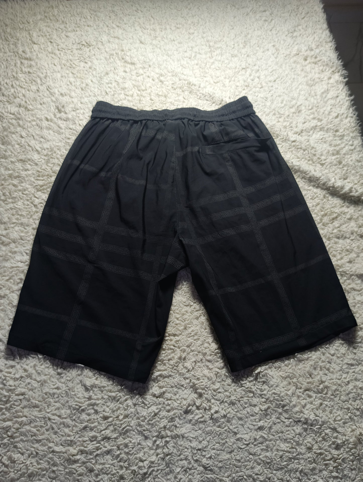 Black plaid shorts with an elastic waistband, laid flat on a textured white carpet.
