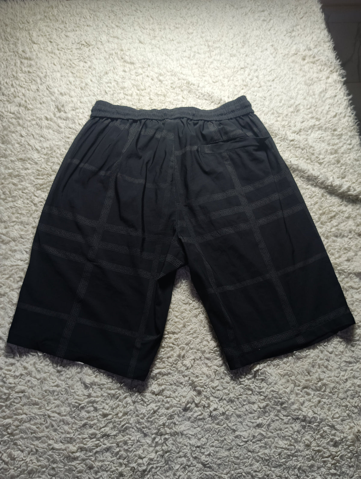 Black plaid shorts with an elastic waistband, laid flat on a textured white carpet.