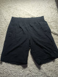 Black athletic shorts with an elastic waistband, laid flat on a white shag carpet.