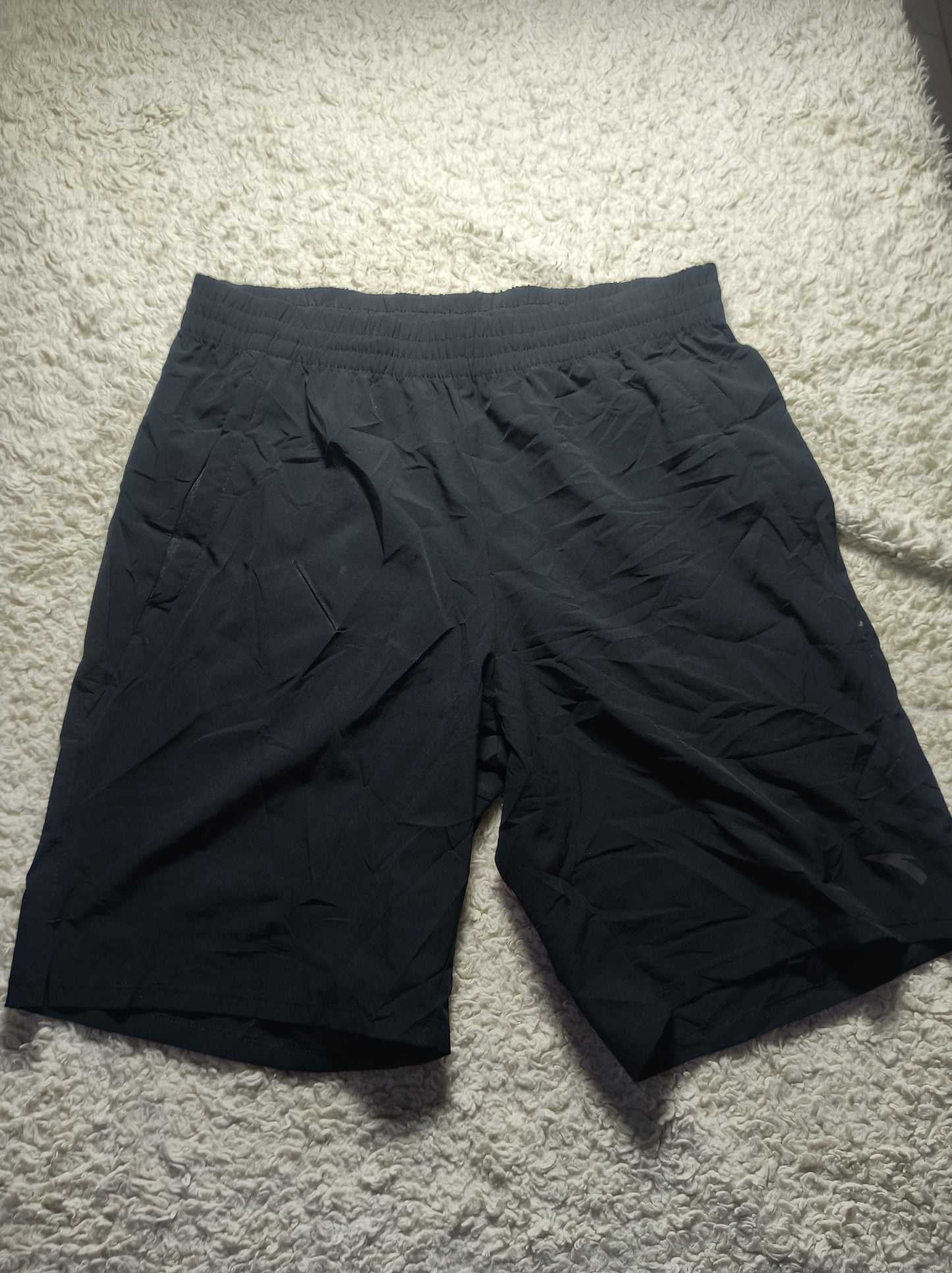 Black athletic shorts with an elastic waistband, laid flat on a white shag carpet.