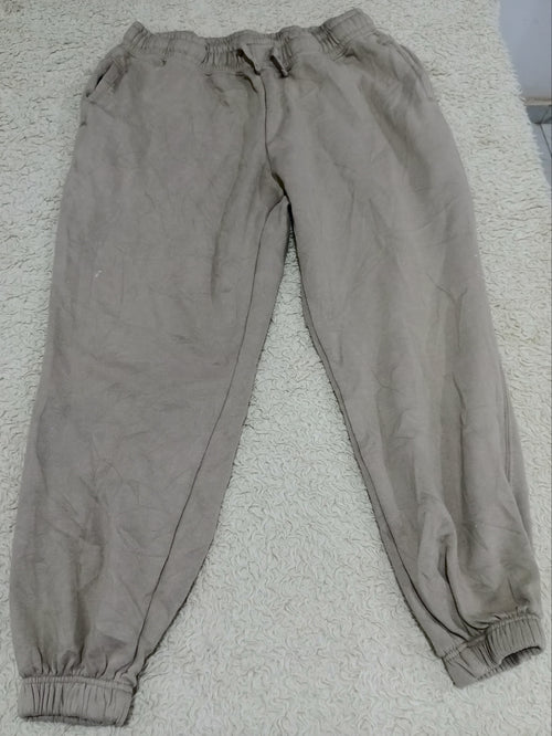 A pair of light brown or taupe jogger pants laid flat on a textured white carpet. The pants feature an elastic waistband with a drawstring, side pockets, and elastic cuffs at the ankles.