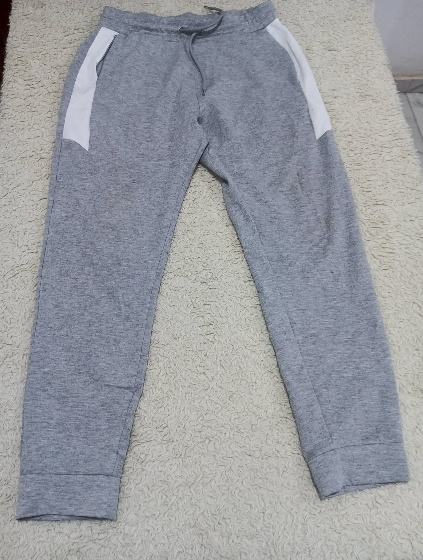 A pair of heather gray sweatpants with white side panels, laid flat on a textured beige carpet.