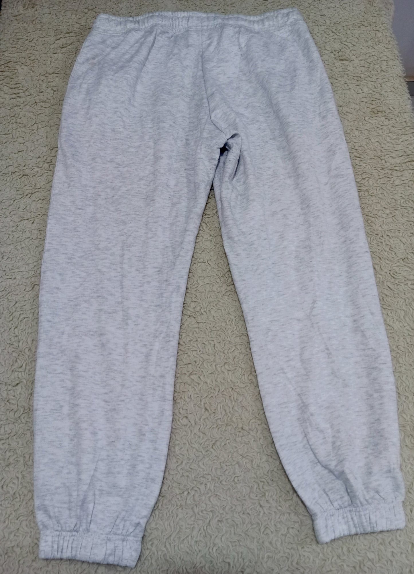 Light gray heather sweatpants with an elastic waistband and ribbed ankle cuffs, laid flat on a beige carpet.