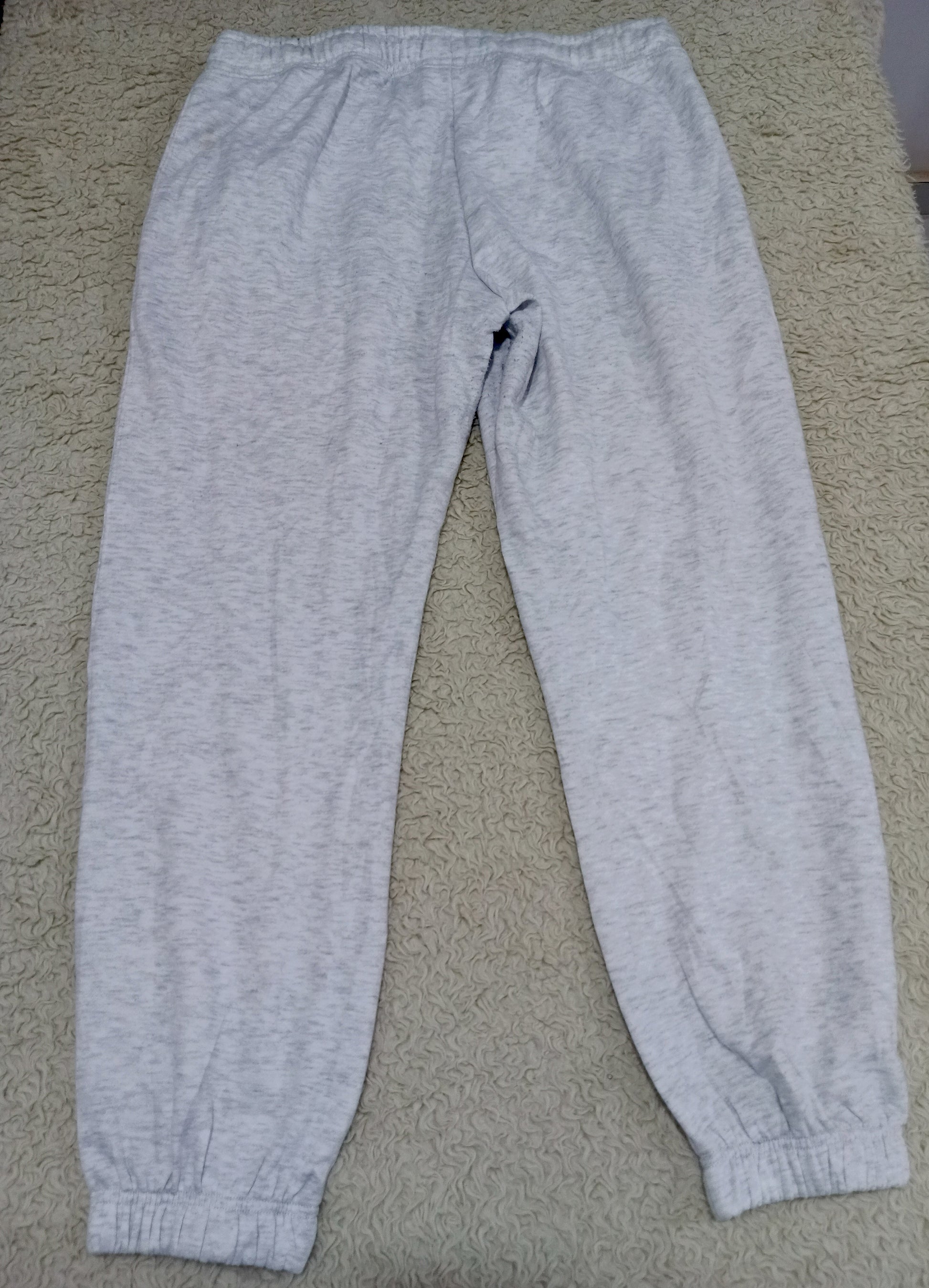 Light gray heather sweatpants with an elastic waistband and ribbed ankle cuffs, laid flat on a beige carpet.
