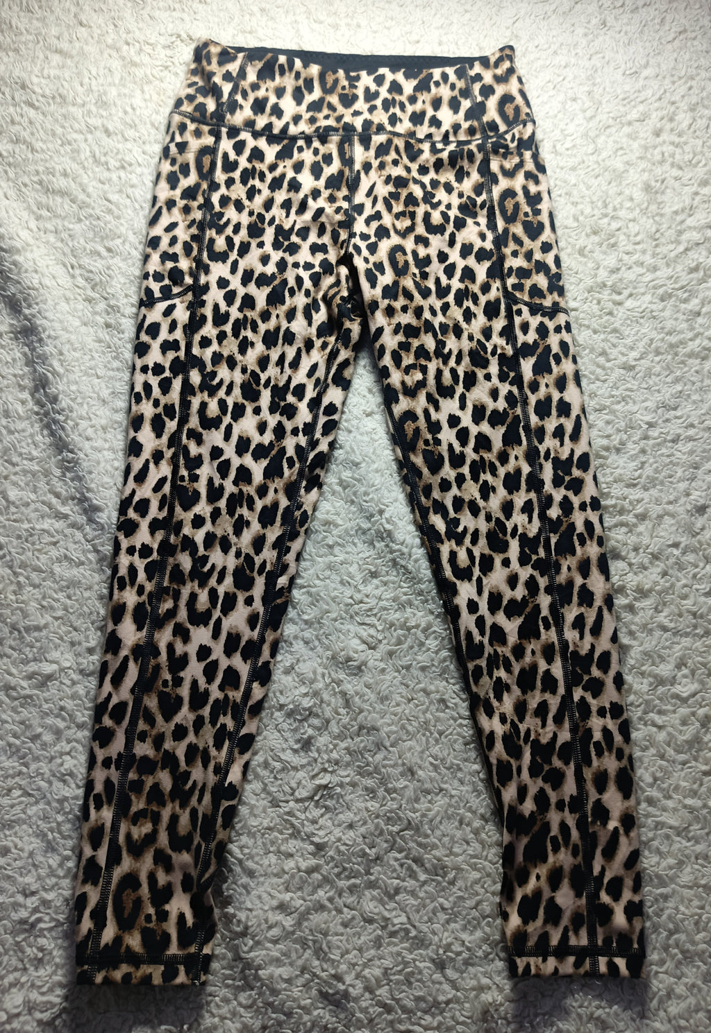 Leopard print leggings laid flat on a gray textured rug. The leggings feature a classic leopard pattern with black spots on a tan and brown base.