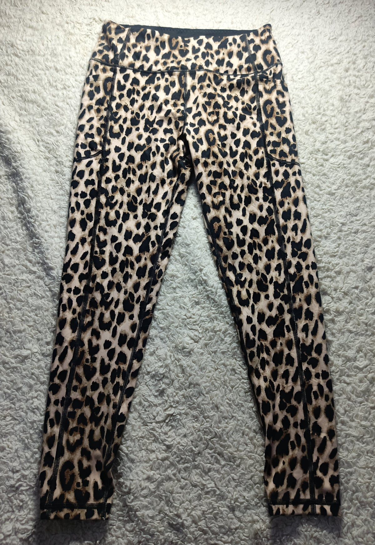 Leopard print leggings laid flat on a gray textured rug. The leggings feature a classic leopard pattern with black spots on a tan and brown base.