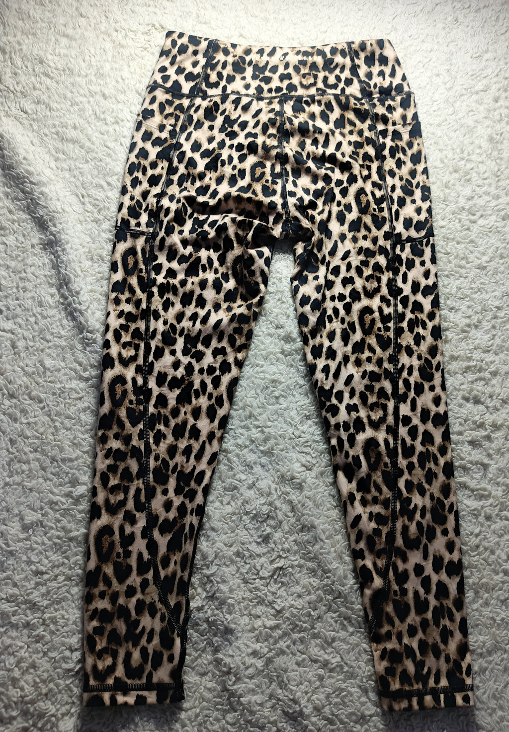 Leopard print leggings laid flat on a gray textured surface, featuring a classic animal spot pattern in black, brown, and beige tones.