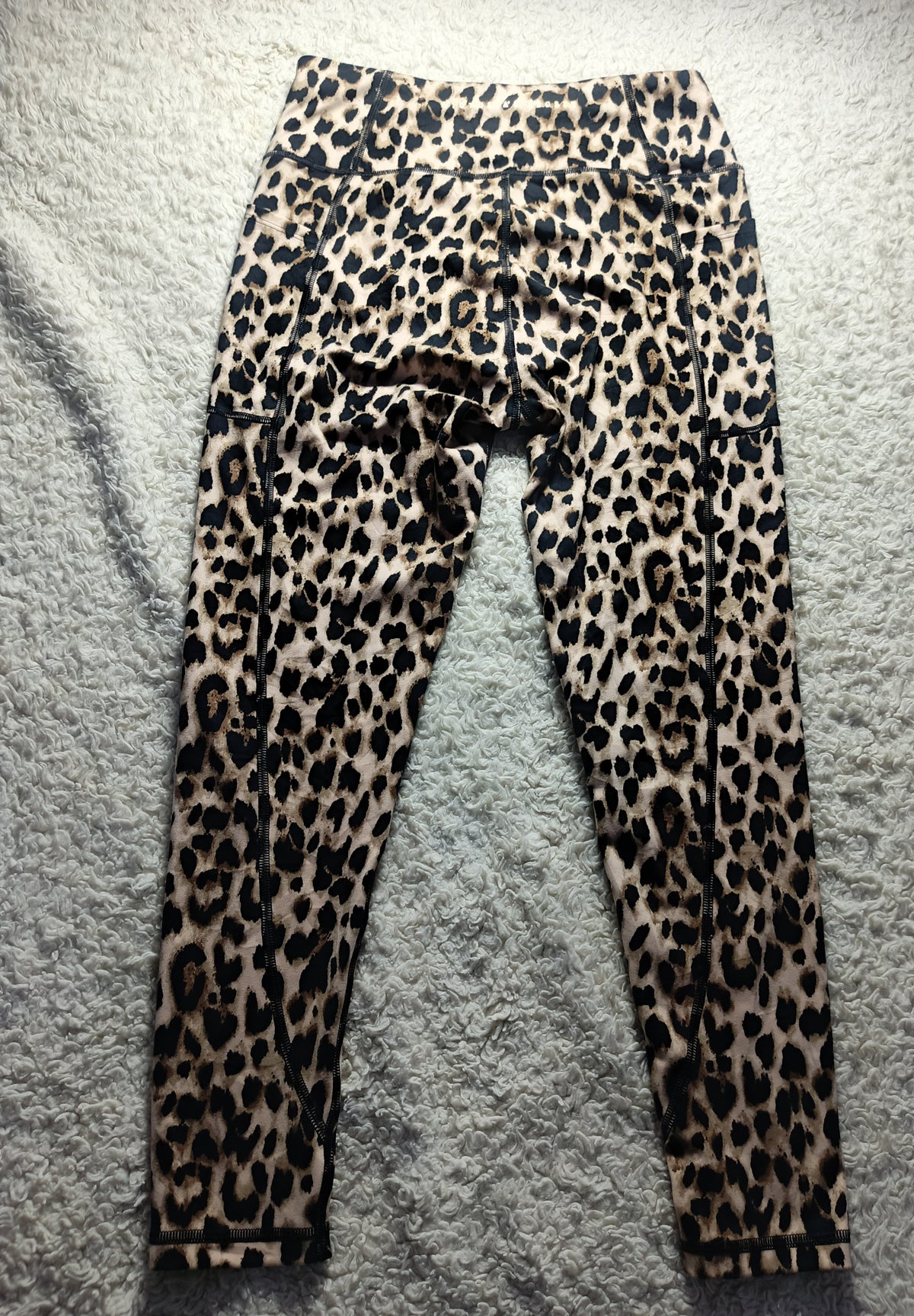 Leopard print leggings laid flat on a gray textured surface, featuring a classic animal spot pattern in black, brown, and beige tones.