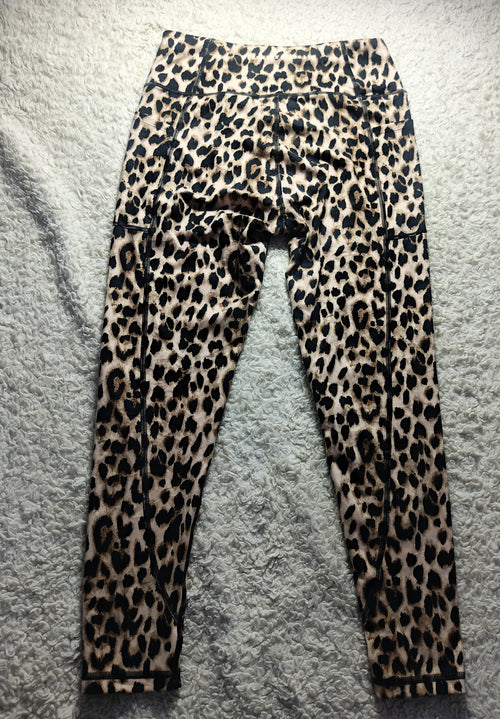 Leopard print leggings laid flat on a gray textured surface, featuring a classic animal spot pattern in black, brown, and beige tones.