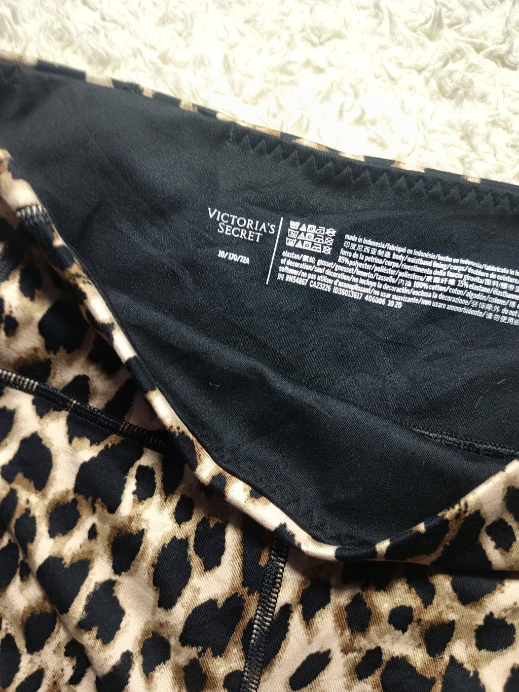 Close-up of a leopard print garment with a black inner lining and visible Victoria's Secret branding on the inside neck label.