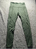 A pair of high-waisted, form-fitting leggings in a heathered sage green color, laid flat on a textured gray carpet.