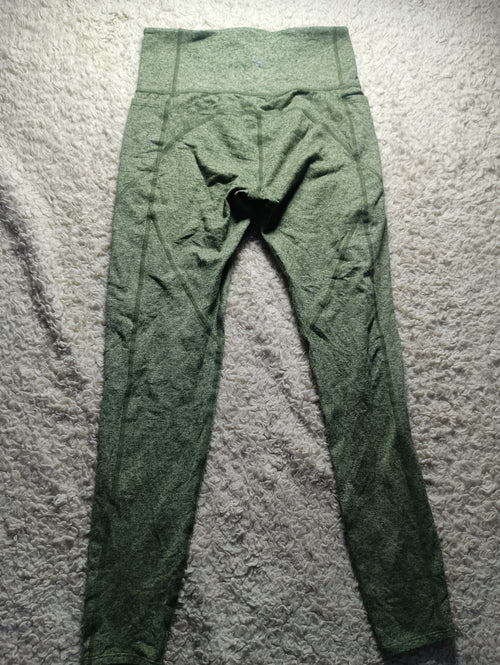 A pair of olive green high-waisted leggings laid flat on a textured gray carpet. The image has a white border at the bottom with camera metadata 'POVA & Neo 23mm f/1.
