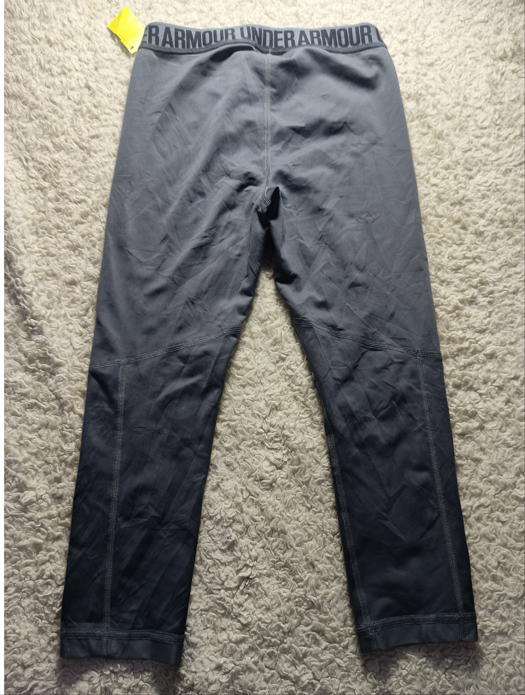 Dark gray athletic leggings laid flat on a beige carpet, with the waistband showing the brand name 'BARMENDES' and a small yellow price tag attached near the left hip.