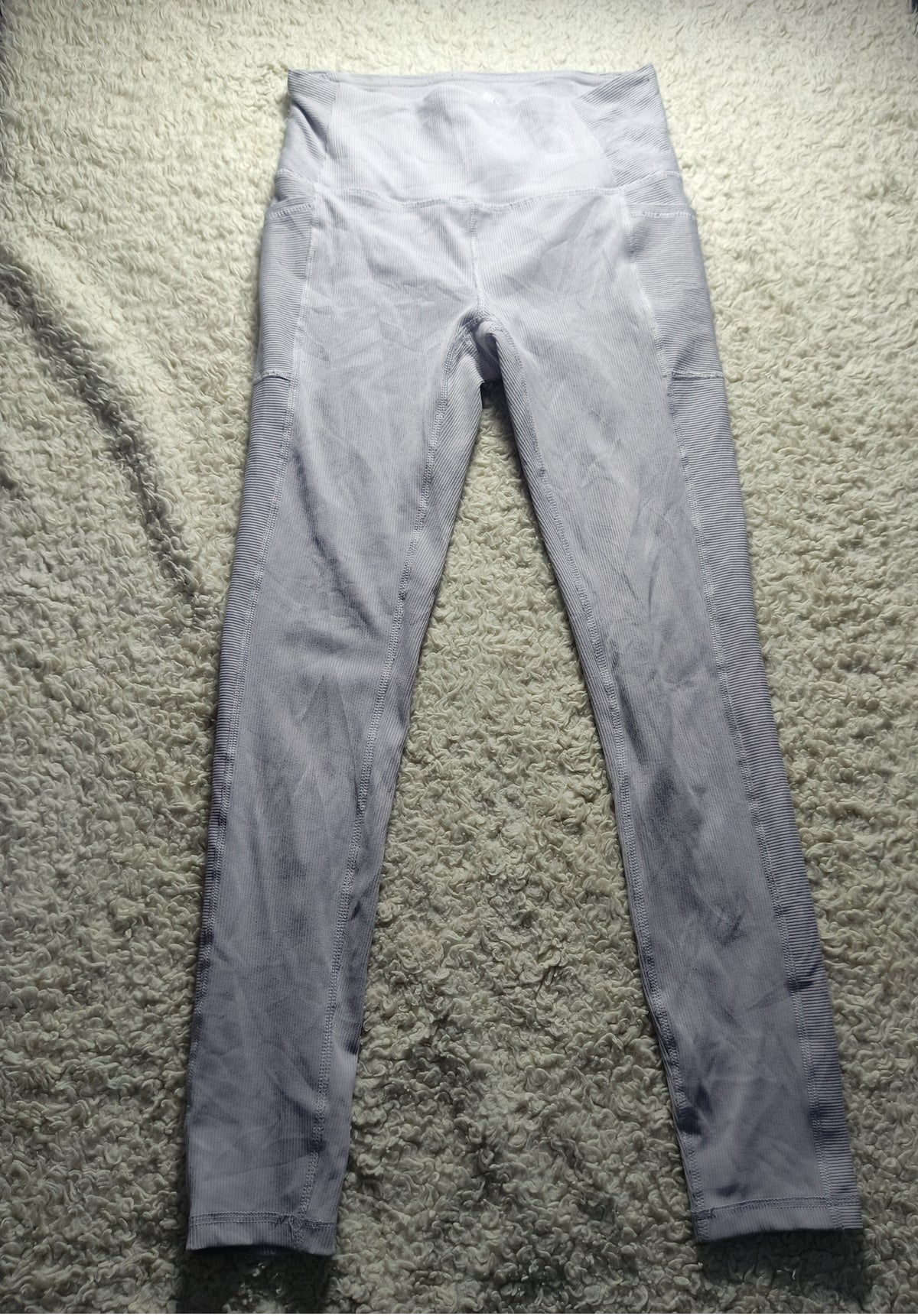 A pair of light gray high-waisted leggings laid flat on a textured beige carpet. The photo is taken from a top-down angle with a camera watermark at the bottom showing 'POVA 6 Neo' and camera settings.