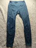 A pair of dark teal athletic leggings laid flat on a textured beige carpet. The leggings feature a smooth upper body and textured, ribbed knee panels.