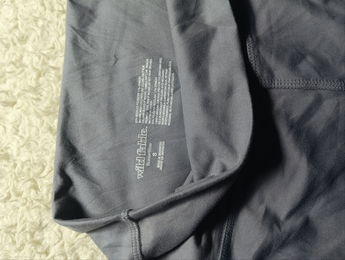 Close-up of a dark gray athletic garment laid flat, showing the inner label area and stitched seam details, photographed on a light textured surface.