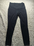 Black leggings laid flat on a textured beige carpet, photographed from above with a camera watermark at the bottom.