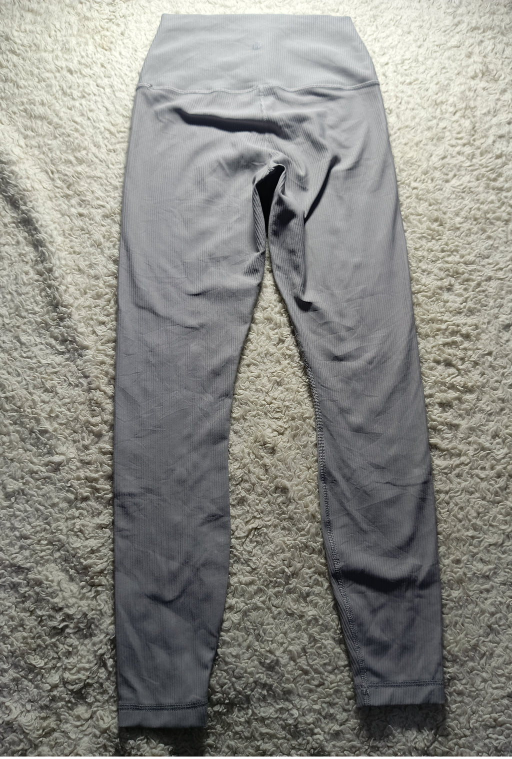 A pair of high-waisted gray leggings laid flat on a textured gray shag rug, photographed from the back. The image has camera metadata watermarks at the bottom.