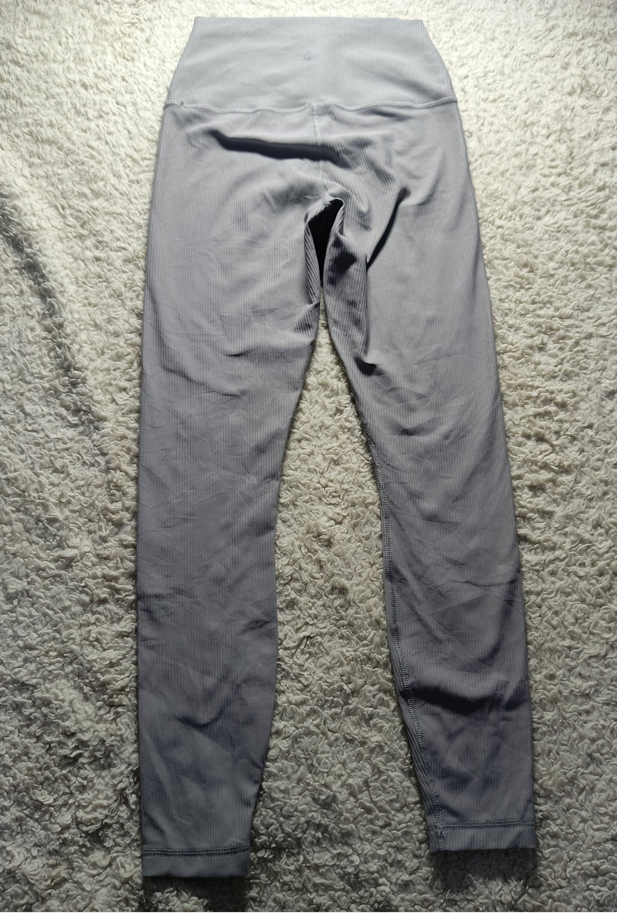 A pair of high-waisted gray leggings laid flat on a textured gray shag rug, photographed from the back. The image has camera metadata watermarks at the bottom.