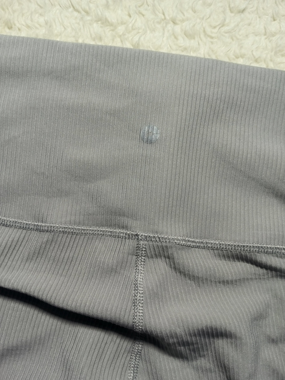Close-up of a pair of gray ribbed athletic leggings or shorts showing the waistband stitching and leg seam, laid flat on a textured cream surface.