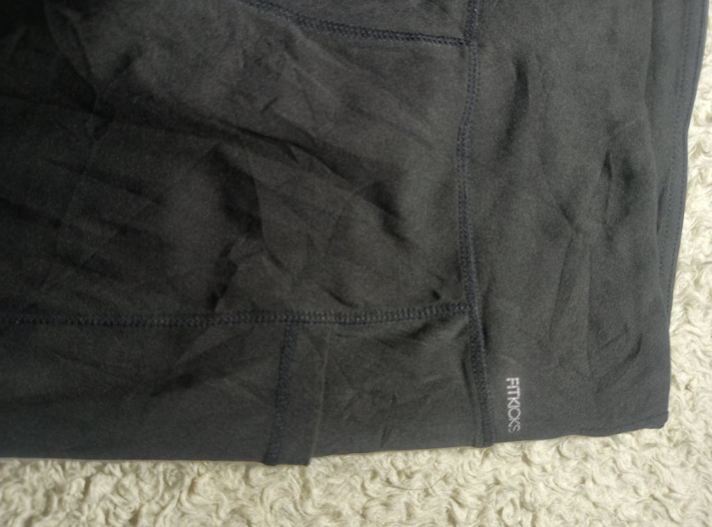 A close-up of dark charcoal gray athletic shorts with visible stitching and a small white 'FROGS' brand logo near the lower right hem, laid flat on a textured cream carpet.