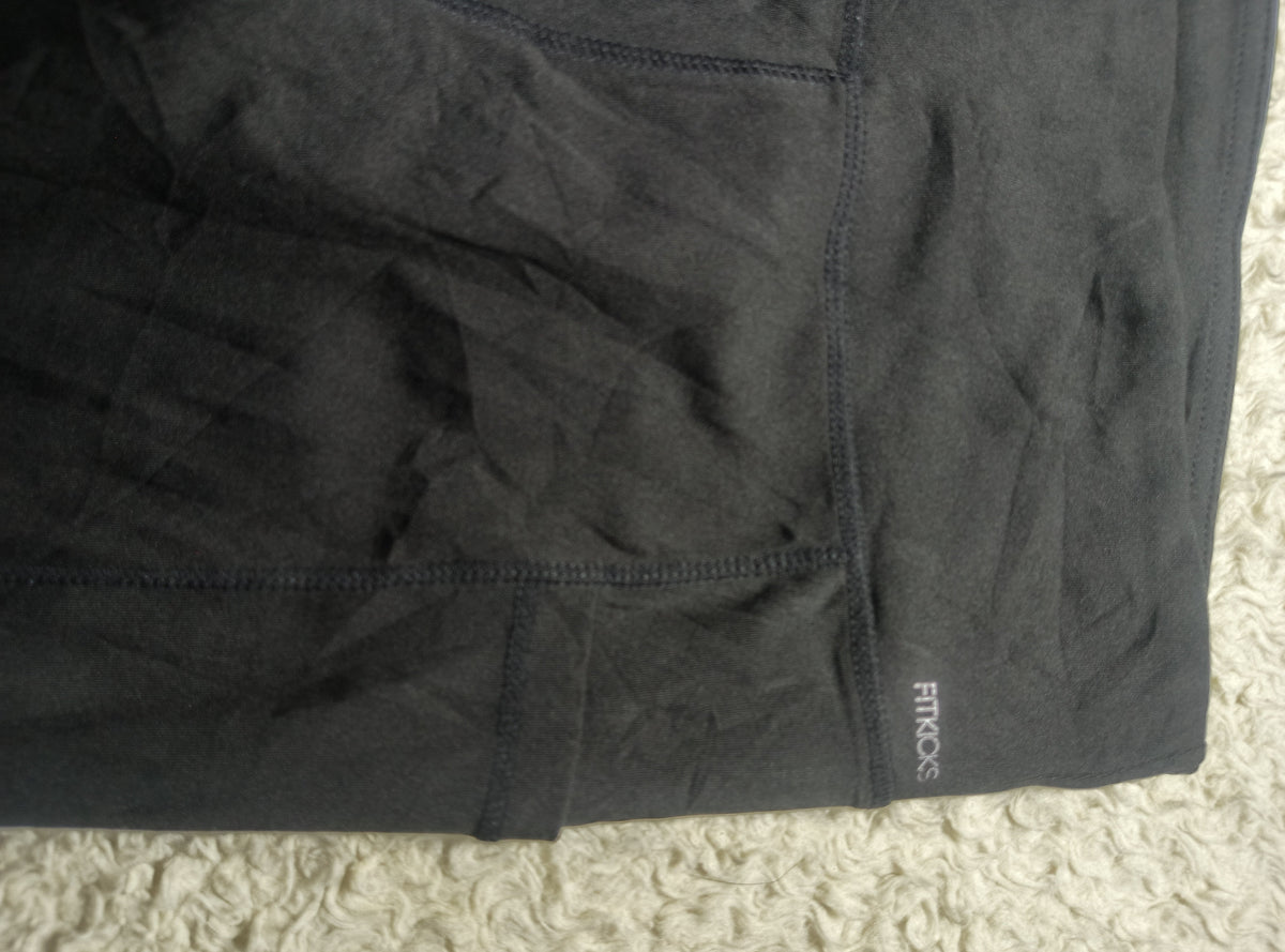 A close-up of dark charcoal gray athletic shorts with visible stitching and a small white 'FROGS' brand logo near the lower right hem, laid flat on a textured cream carpet.