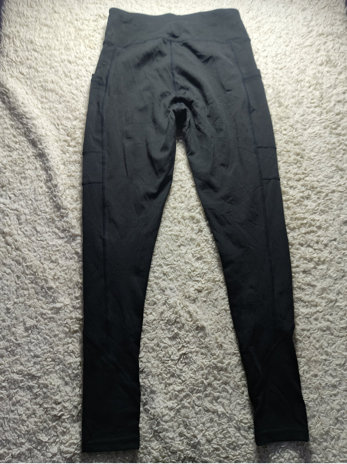Black high-waisted athletic leggings laid flat on a textured gray carpet background.
