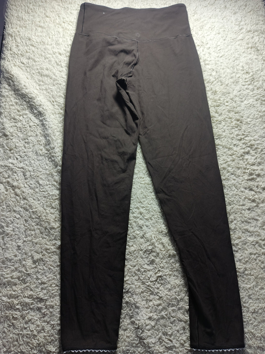 A pair of dark brown or very deep charcoal leggings laid flat on a textured gray carpet. The image has camera metadata text overlaid at the bottom.