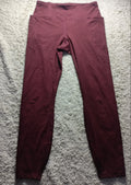 A pair of high-waisted leggings in a deep burgundy or maroon color, laid flat on a textured gray carpet. The image has a camera watermark at the bottom.