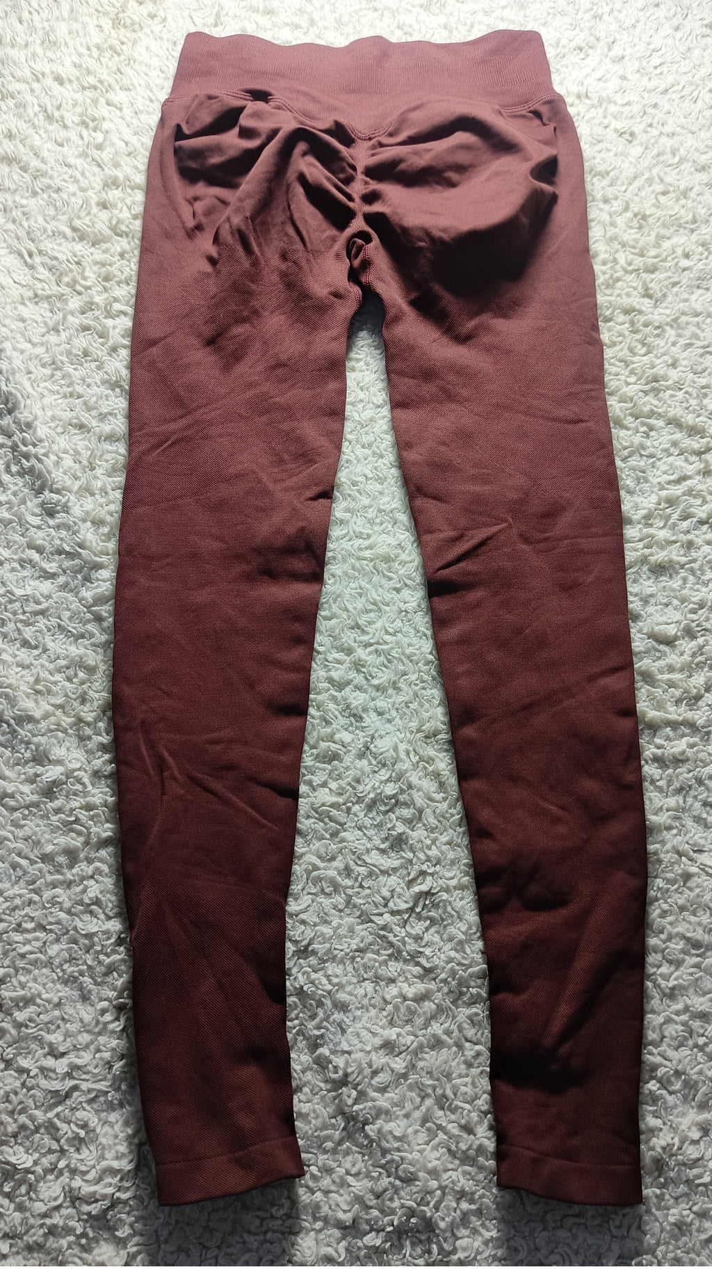 A pair of dark reddish-brown leggings laid flat on a textured gray carpet, featuring a gathered ruched waistband.