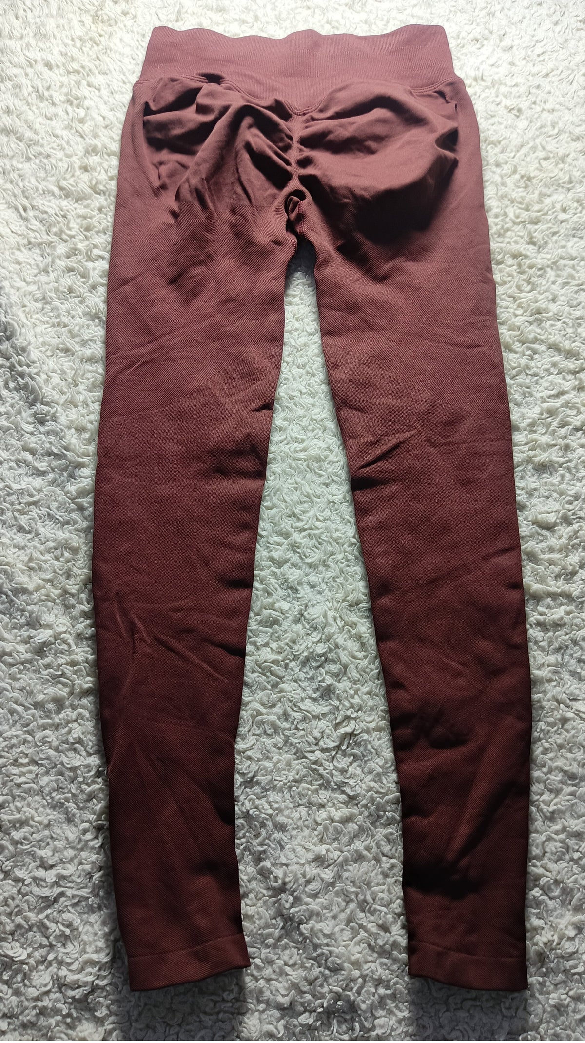 A pair of dark reddish-brown leggings laid flat on a textured gray carpet, featuring a gathered ruched waistband.