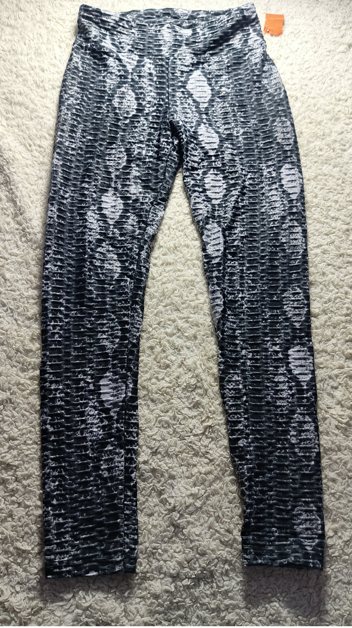 Black and white snakeskin print leggings laid flat on a textured beige carpet, with an orange tag visible at the waistband.