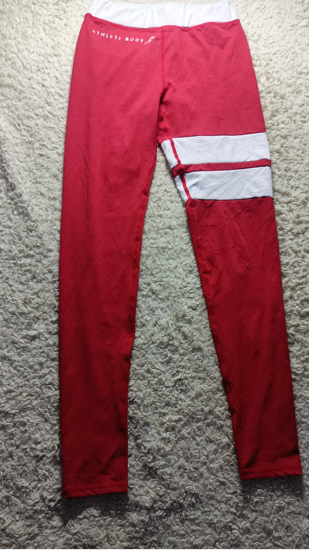 Red athletic leggings with a white contrast panel and white stripes on the right leg, laid flat on a gray shag carpet.