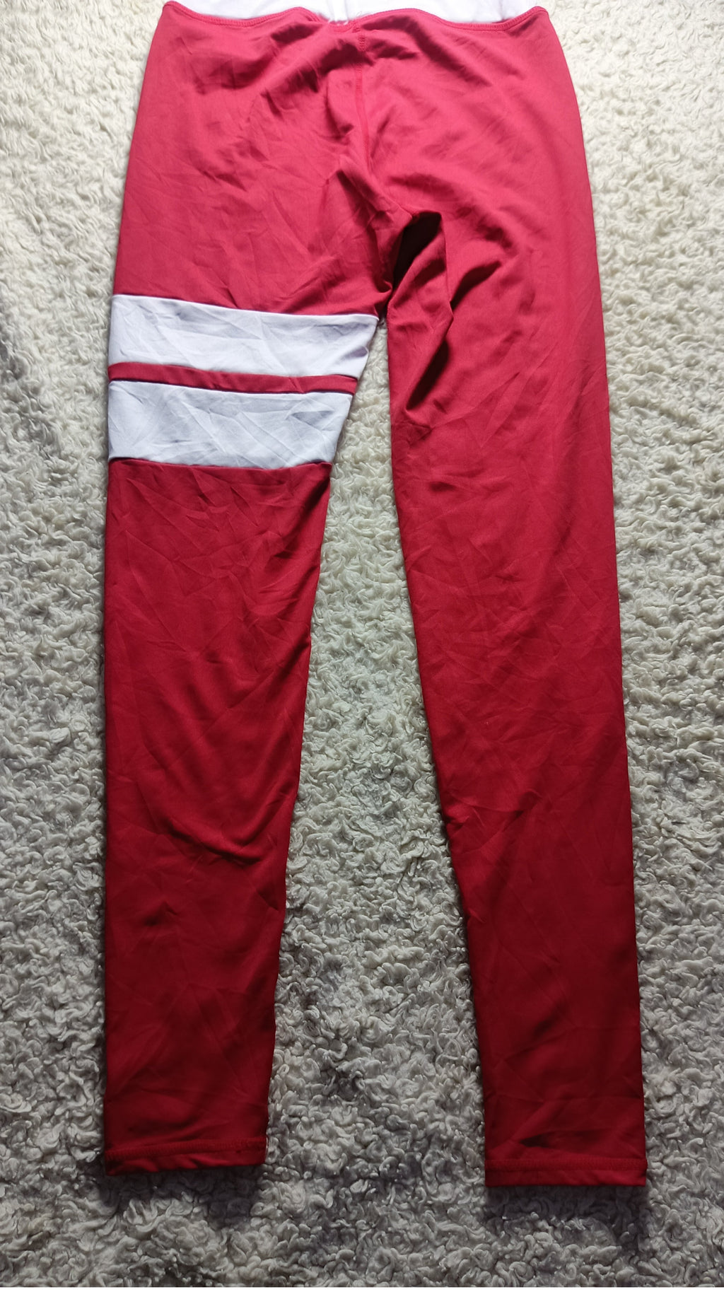Red athletic leggings with a white stripe detail on the upper left leg, laid flat on a gray textured carpet.
