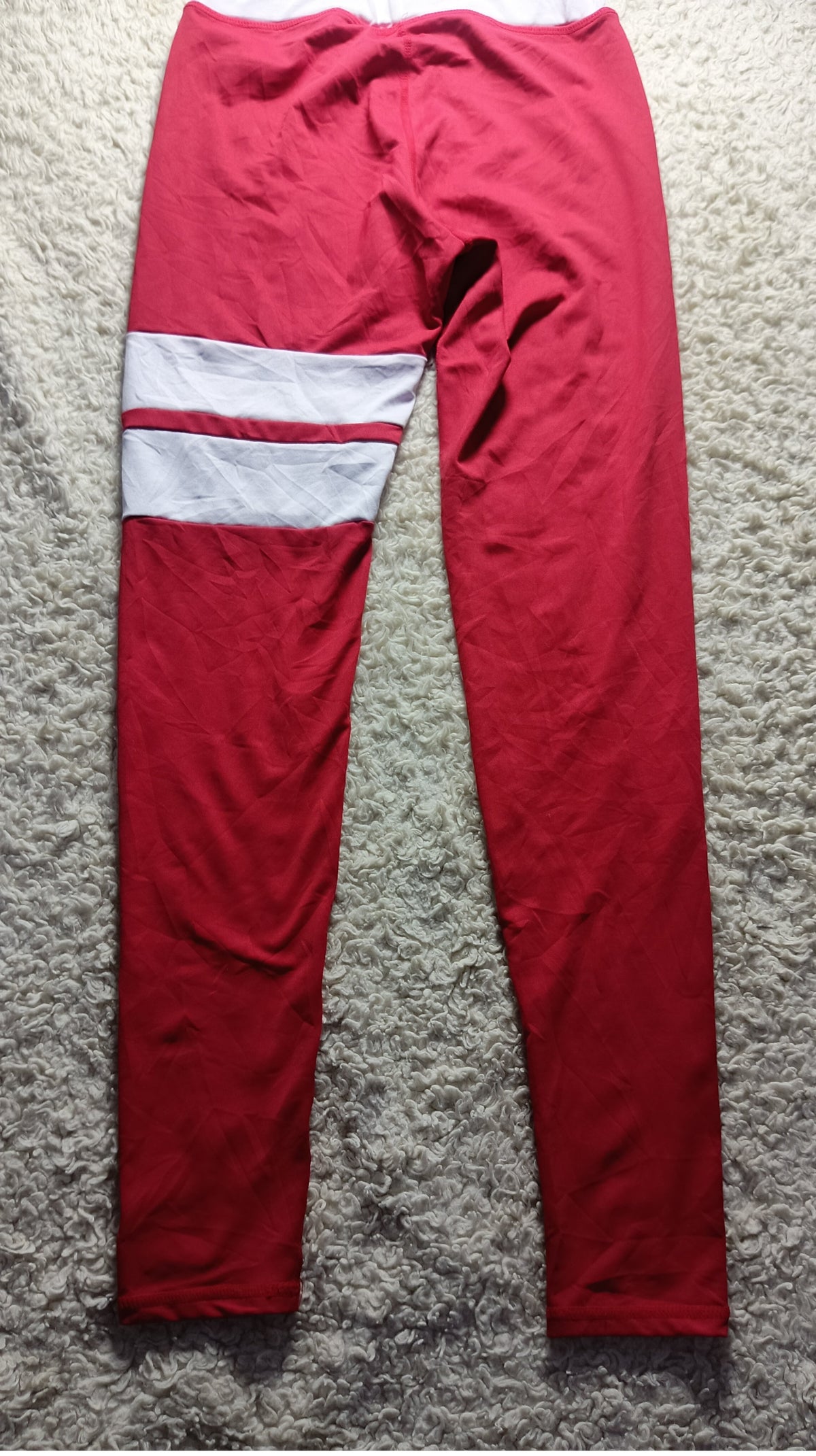 Red athletic leggings with a white stripe detail on the upper left leg, laid flat on a gray textured carpet.