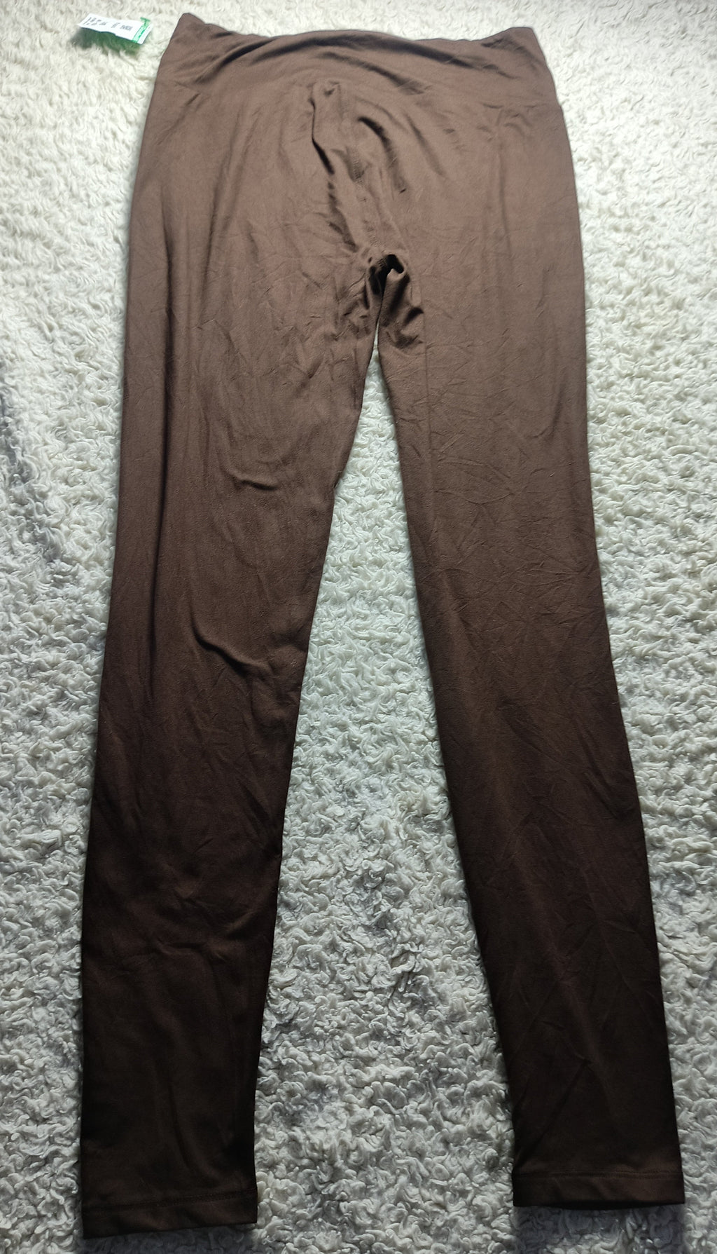 A pair of solid brown leggings laid flat on a textured gray carpet.