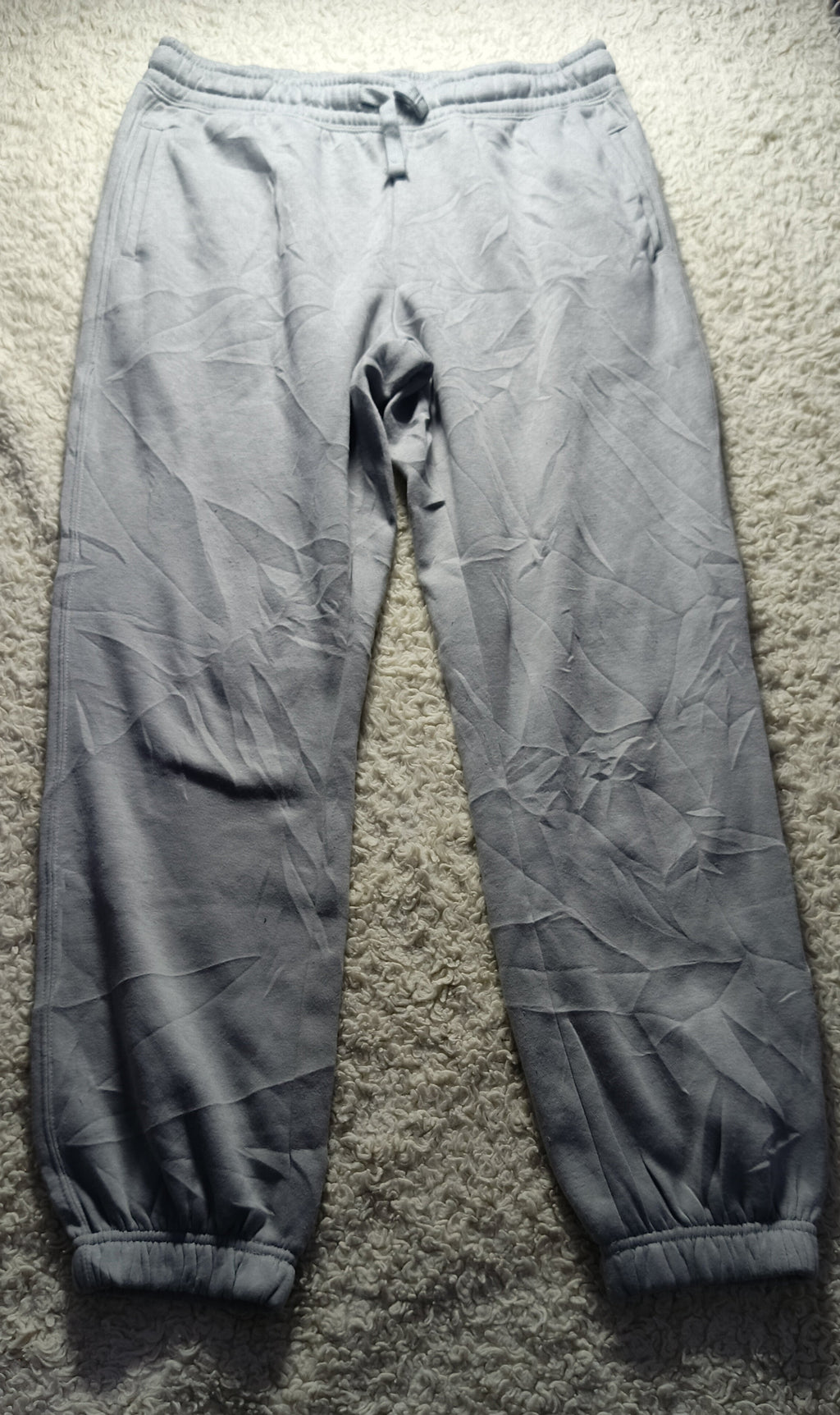 A pair of light gray jogger pants laid flat on a textured gray carpet. The pants have a drawstring waist, elastic cuffs, and a wrinkled, creased texture.