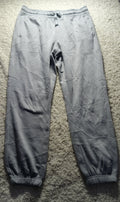 A pair of light gray jogger pants laid flat on a textured gray carpet. The pants have a drawstring waist, elastic cuffs, and a wrinkled, creased texture.