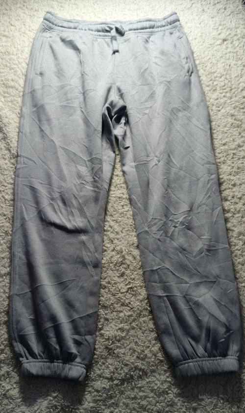 A pair of light gray jogger pants laid flat on a textured gray carpet. The pants have a drawstring waist, elastic cuffs, and a wrinkled, creased texture.