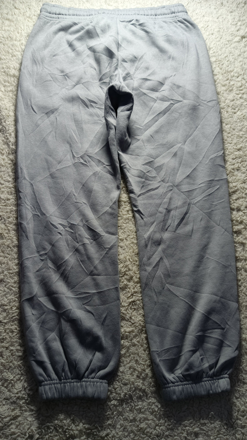 A pair of gray jogger pants laid flat on a textured gray carpet, showing a loose fit and elastic cuffs.