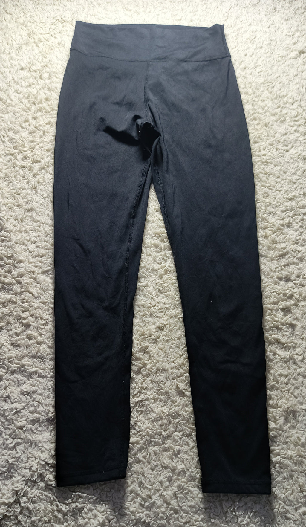 Black high-waisted leggings laid flat on a textured gray shag rug.