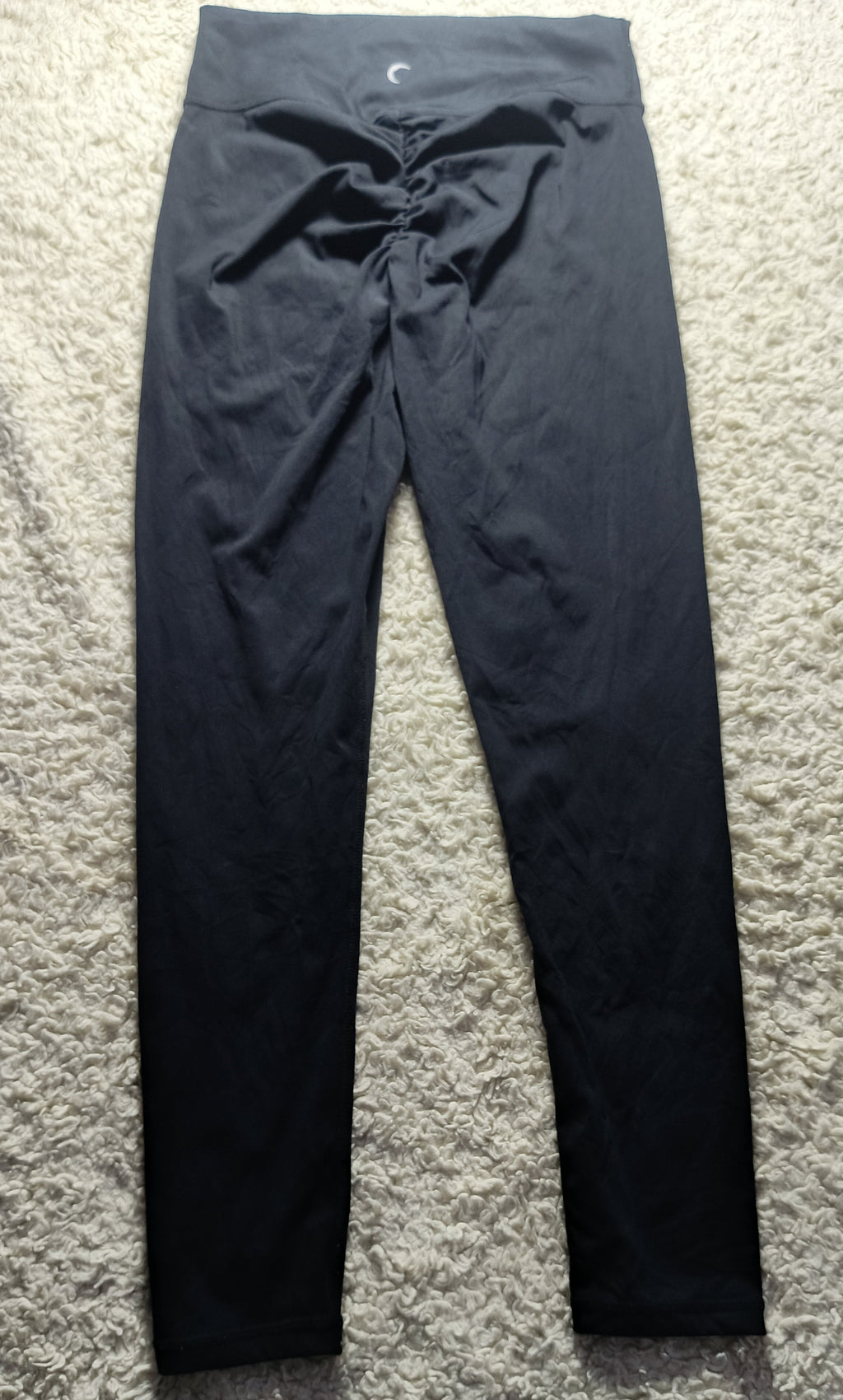 Black high-waisted leggings with a drawstring waist, laid flat on a textured gray carpet.