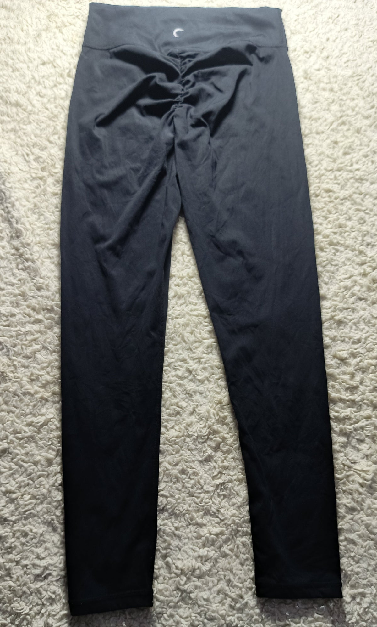 Black high-waisted leggings with a drawstring waist, laid flat on a textured gray carpet.
